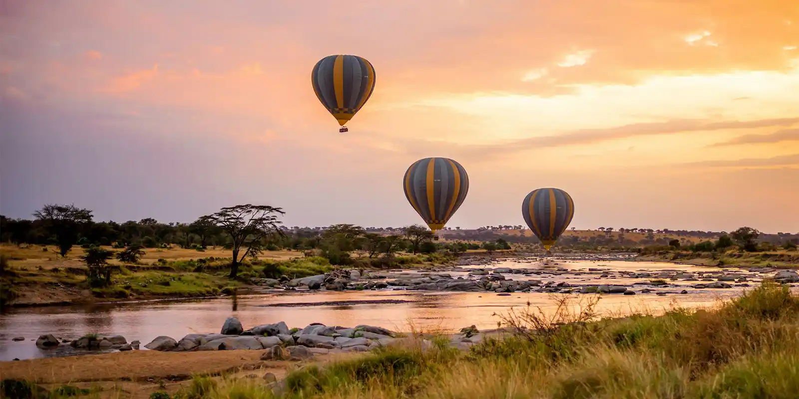 3 hot air balloons flying above a river